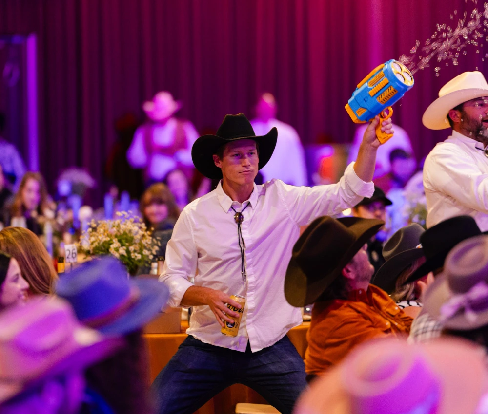 man in cowboy hat with bubble gun pointed at the sky