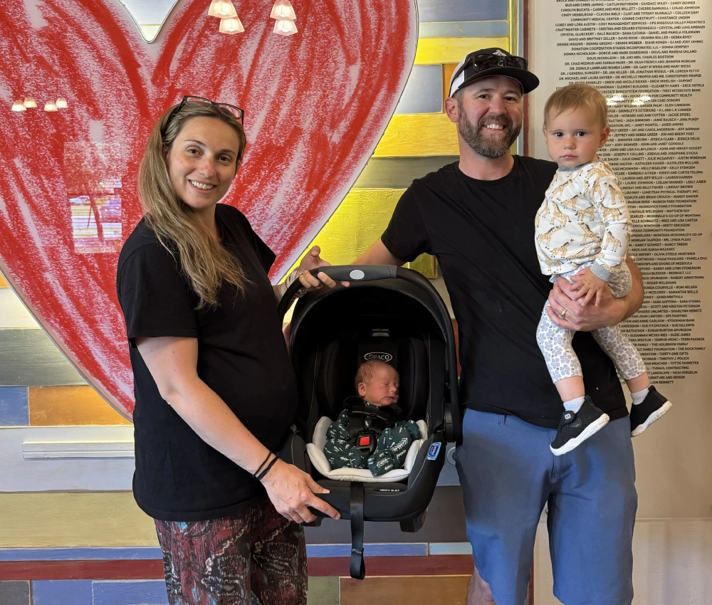 mother father and two young children smiling in front of our heart artwork