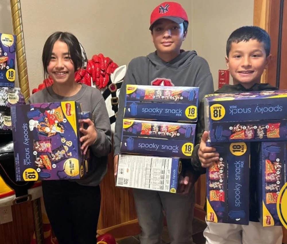three young kids with their arms full of boxes of donated snacks