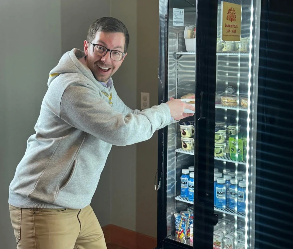 smiling volunteer works to restock a Sunny Start grab and go fridge