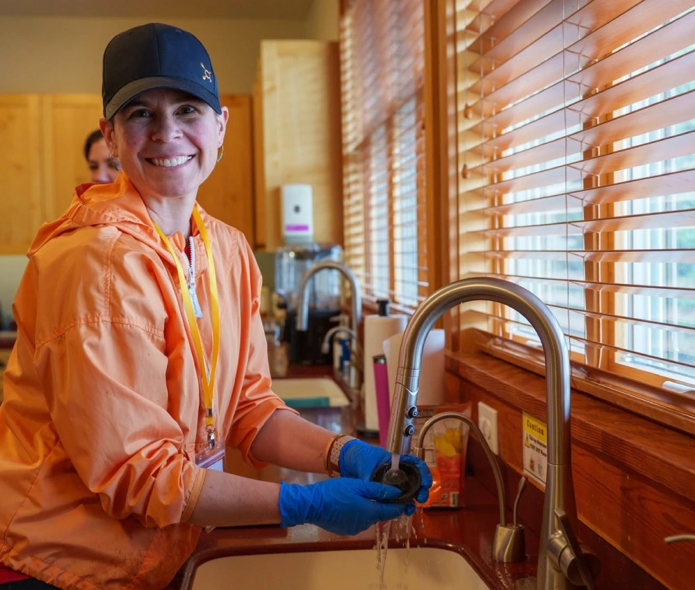 adult female smiling as she's at a sink