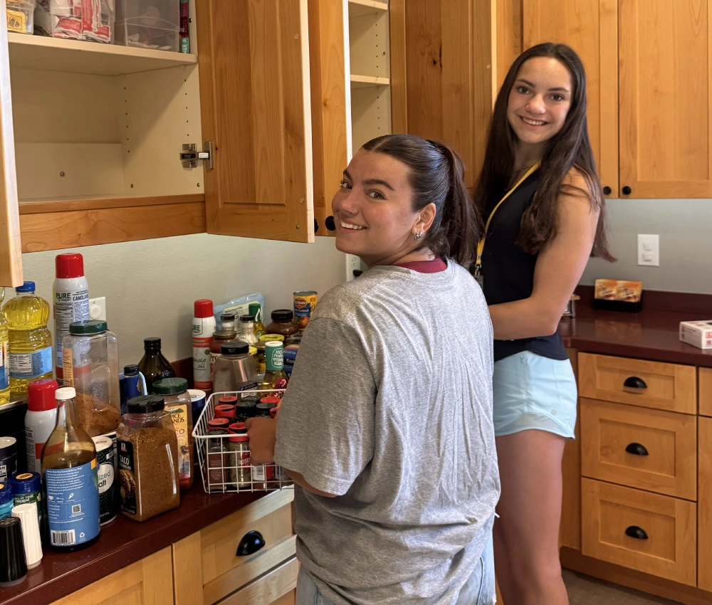 two young adult female volunteers smiling as they work together to organize a cupboard