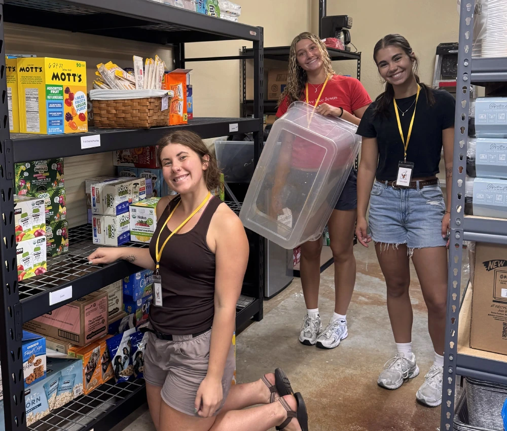 three smiling young women working to stock and organize a storage pantry